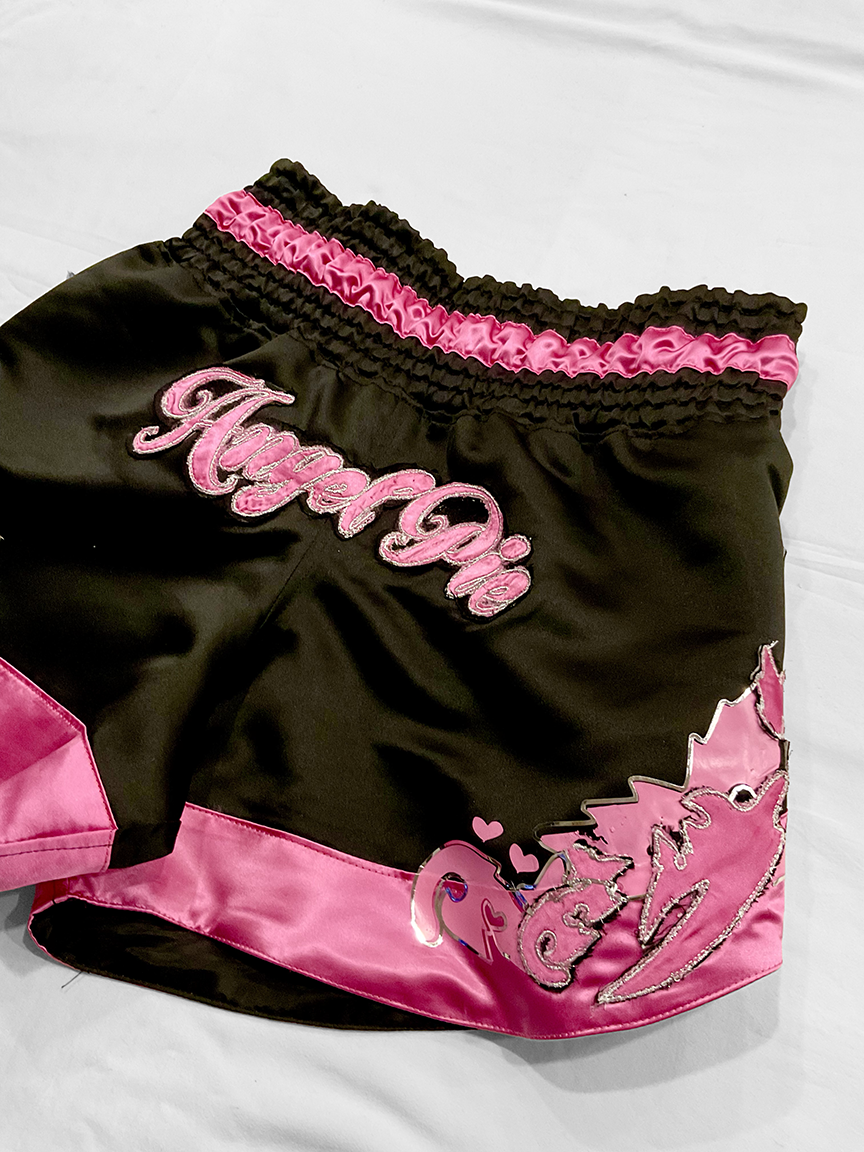 Black & Hot Pink Satin Muay Thai shorts with intricate embroidery & vinyl detail at sides. Angel Pie embroidery on Front